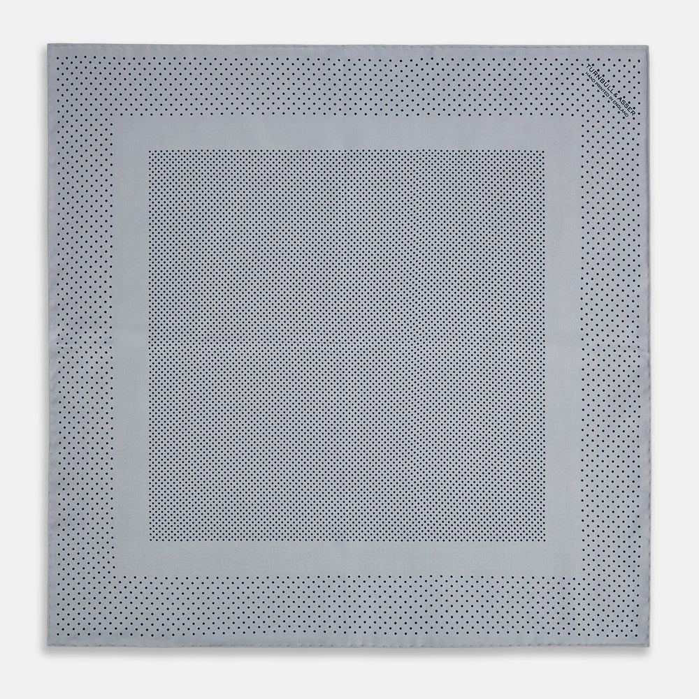 The Turnbull & Asser Grey Dot Silk Pocket Square features a light gray silk design with navy polka dots and a solid border. Elegantly handmade, it is shown with one corner folded to display both sides.