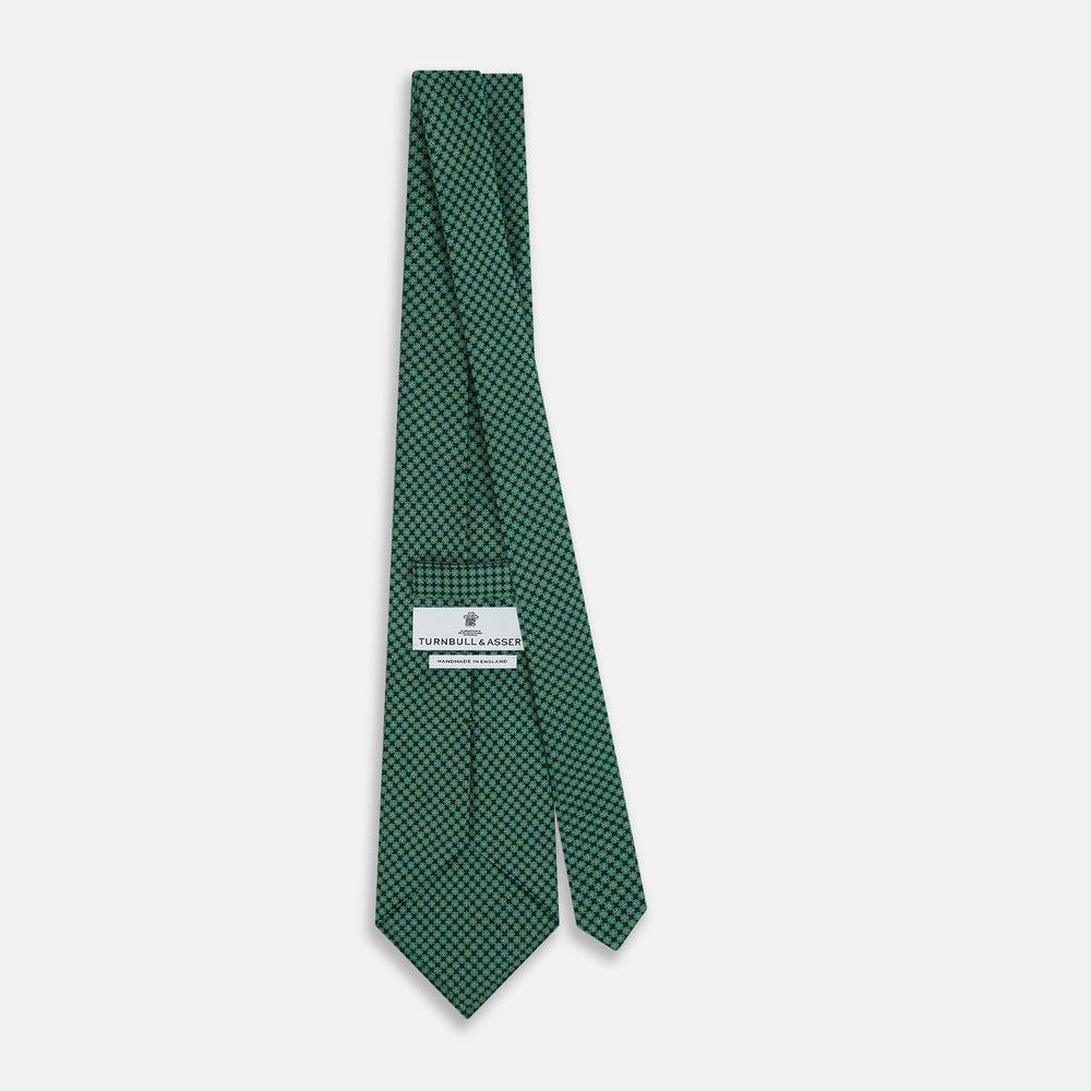 The Forest Green Geometric Floral Printed Silk Tie by Turnbull & Asser is shown rolled up on a white background, its English silk material featuring an elegant green and turquoise pattern.