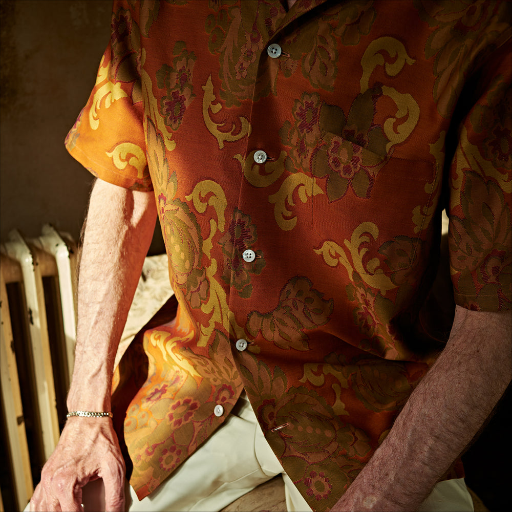 The Orange & Ochre Tapestry Weave Cotton Holiday Fit Shirt by Turnbull & Asser is a short-sleeve, revere collar shirt featuring a yellow and brown floral and leaf pattern on an orange base, finished with white buttons.