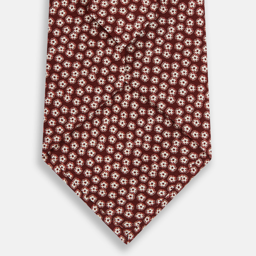 The Turnbull & Asser Burgundy Flower Patterned Silk Tie features a repeating white and light pink floral motif, shown against a plain white background.