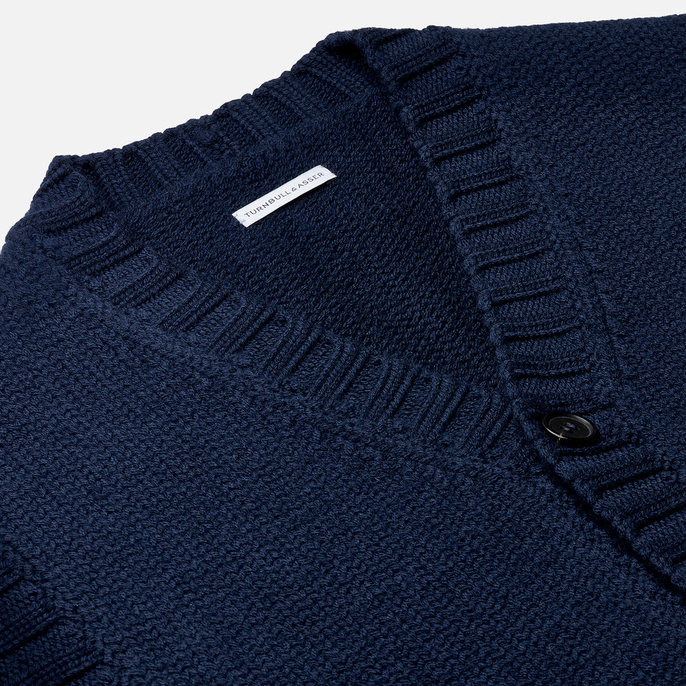 The NAVY MERINO V-NECK SLEEVELESS CARDIGAN by Turnbull & Asser features a button-down front, ribbed edges, and two front pockets—an elegant layering piece for stylish menswear.