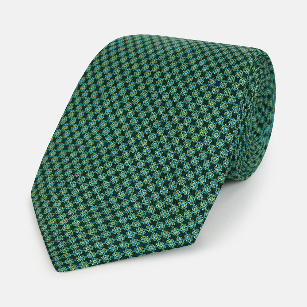 The Forest Green Geometric Floral Printed Silk Tie by Turnbull & Asser is shown rolled up on a white background, its English silk material featuring an elegant green and turquoise pattern.