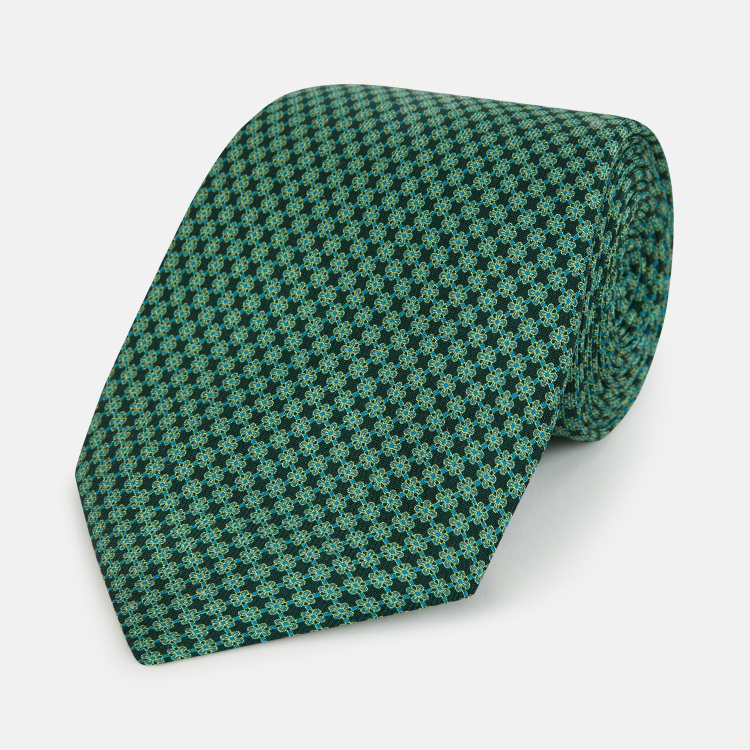 View 1 of product The Forest Green Geometric Floral Printed Silk Tie by Turnbull & Asser is shown rolled up on a white background, its English silk material featuring an elegant green and turquoise pattern.