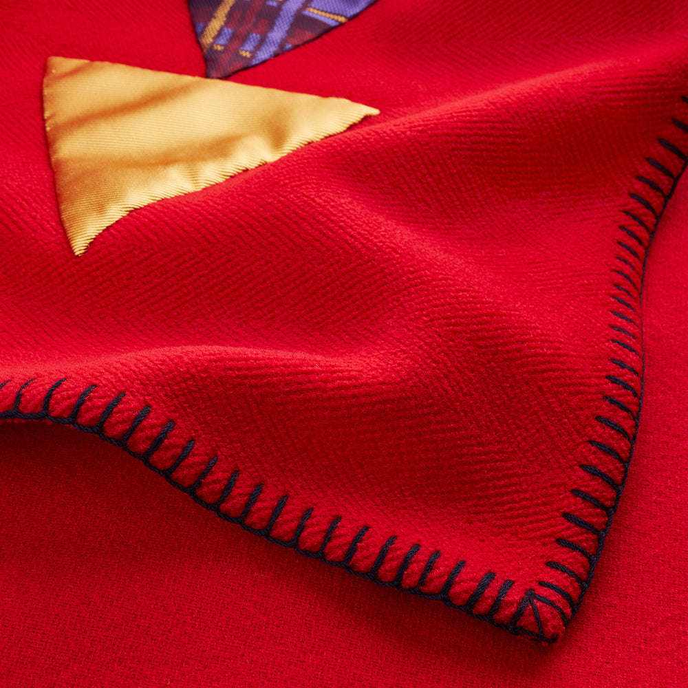 The Turnbull & Asser Red Applique Hand Stitched Lambswool Blanket features black-stitched edges and handsewn tie silk patches, including a yellow triangle and plaid triangle arranged to form a stylized fish.
