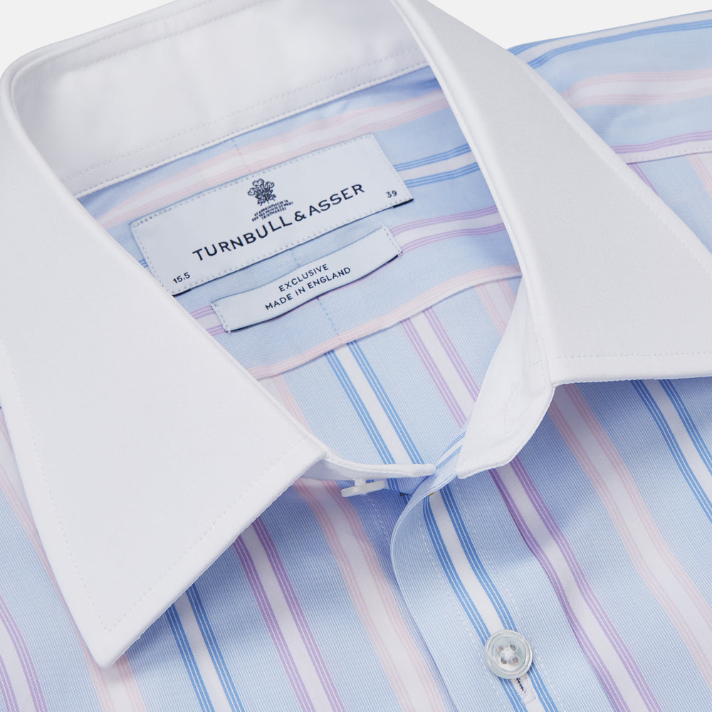 The Turnbull & Asser Light Blue Multi Stripe Cotton Regular Fit Penrose Shirt features light blue, white, and pink stripes with a crisp white collar and cuffs, displayed on a white background.