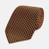 View 1 of product The Turnbull & Asser Orange and Navy Diamond Silk Tie features a yellow and orange diamond pattern on navy silk, ideal for modern office attire, and is displayed rolled up on a light surface.
