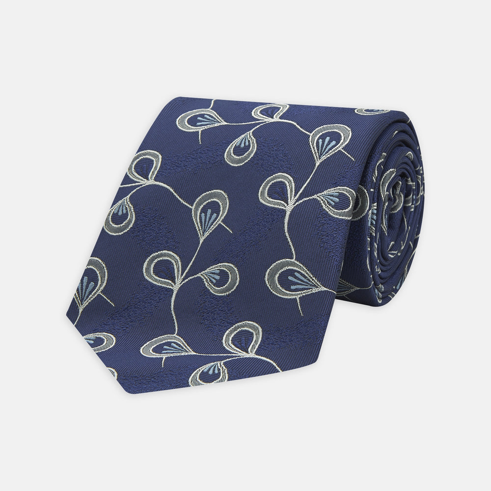 The Turnbull & Asser Navy Jacquard Silk Floral Tie features white and light blue abstract leaf designs, exemplifying fine British craftsmanship. Shown rolled up against a white background.