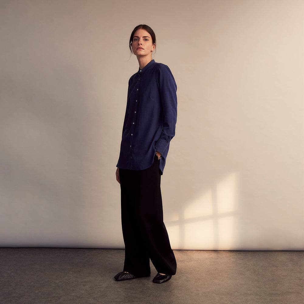 The Turnbull & Asser Blue Soft-touch Silk Lauren Shirt is a navy, long-sleeve button-up with an Igret stand collar, white buttons, curved hem, relaxed fit, and elongated body for a modern look, shown laid flat on a white background.