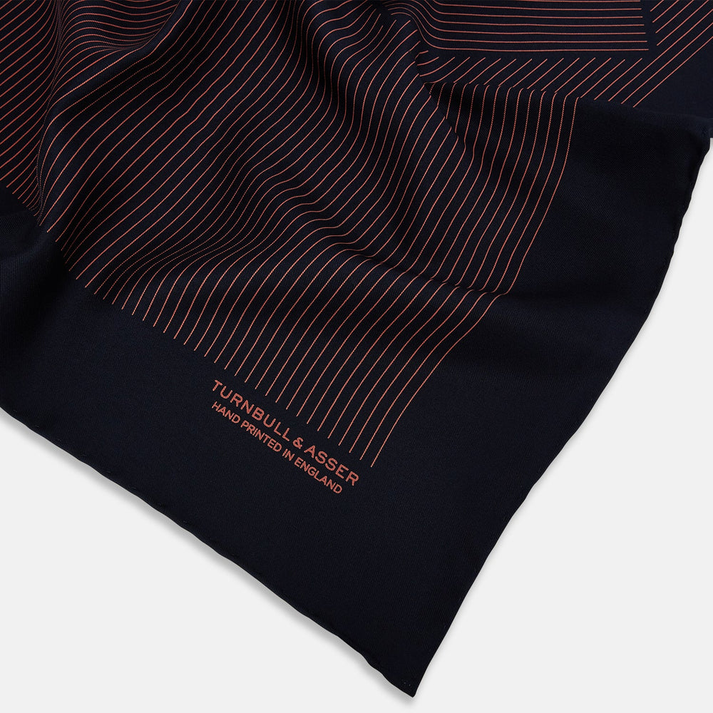 The Navy and Orange Stripe Silk Pocket Square by Turnbull & Asser is handmade in England from silk, featuring thin orange geometric stripes on navy and "Turnbull & Asser Hand Printed in England" printed in the corner.