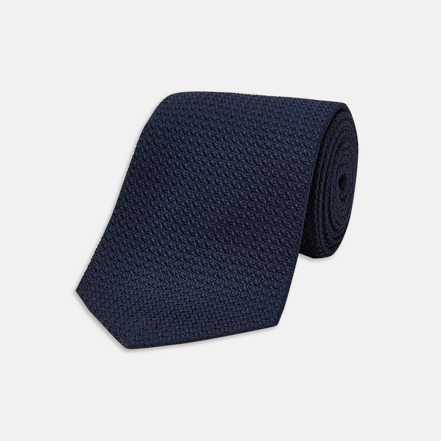 View 1 of product The Turnbull & Asser Navy Plain Woven Grenadine Silk Tie, an essential accessory, is rolled at one end and displayed on a plain white background.