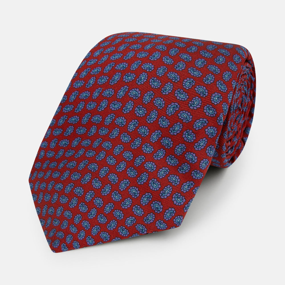 The Turnbull & Asser Red and Purple Miniature Paisley Silk Tie is neatly rolled with the pointed end facing forward.
