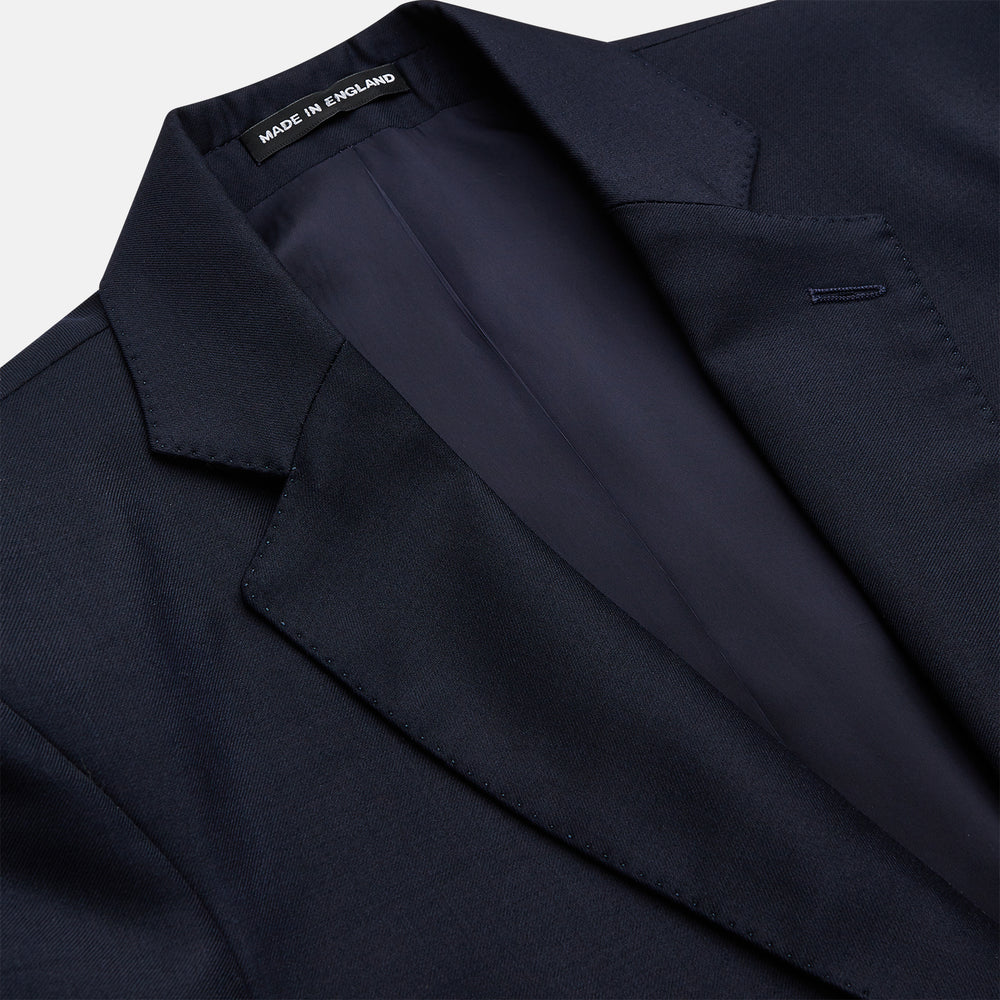 The Turnbull & Asser Navy Plain Wool Single Breasted Blazer, with brass front and cuff buttons and an asymmetric pocket design, is shown laid flat on a white background.