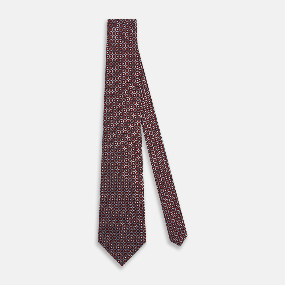 The Turnbull & Asser Burgundy Diamond Silk Tie features a red silk background with a repeating geometric diamond pattern of blue and white squares, exemplifying British craftsmanship.