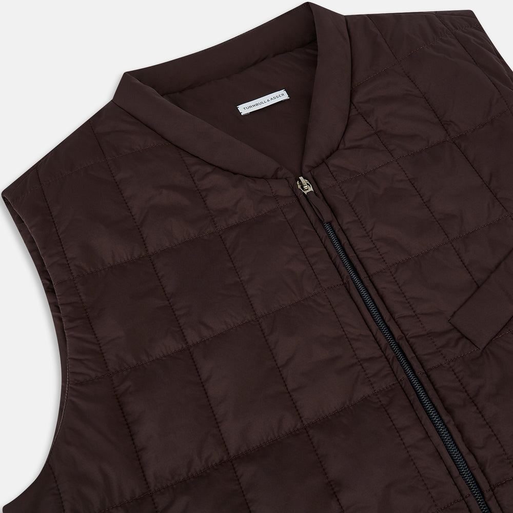 The Turnbull & Asser Burgundy Quilted Gilet is a sleeveless, lightweight layer featuring a front zipper, slanted chest pocket, adjustable side tabs, and two zippered side pockets, shown on a plain white background.