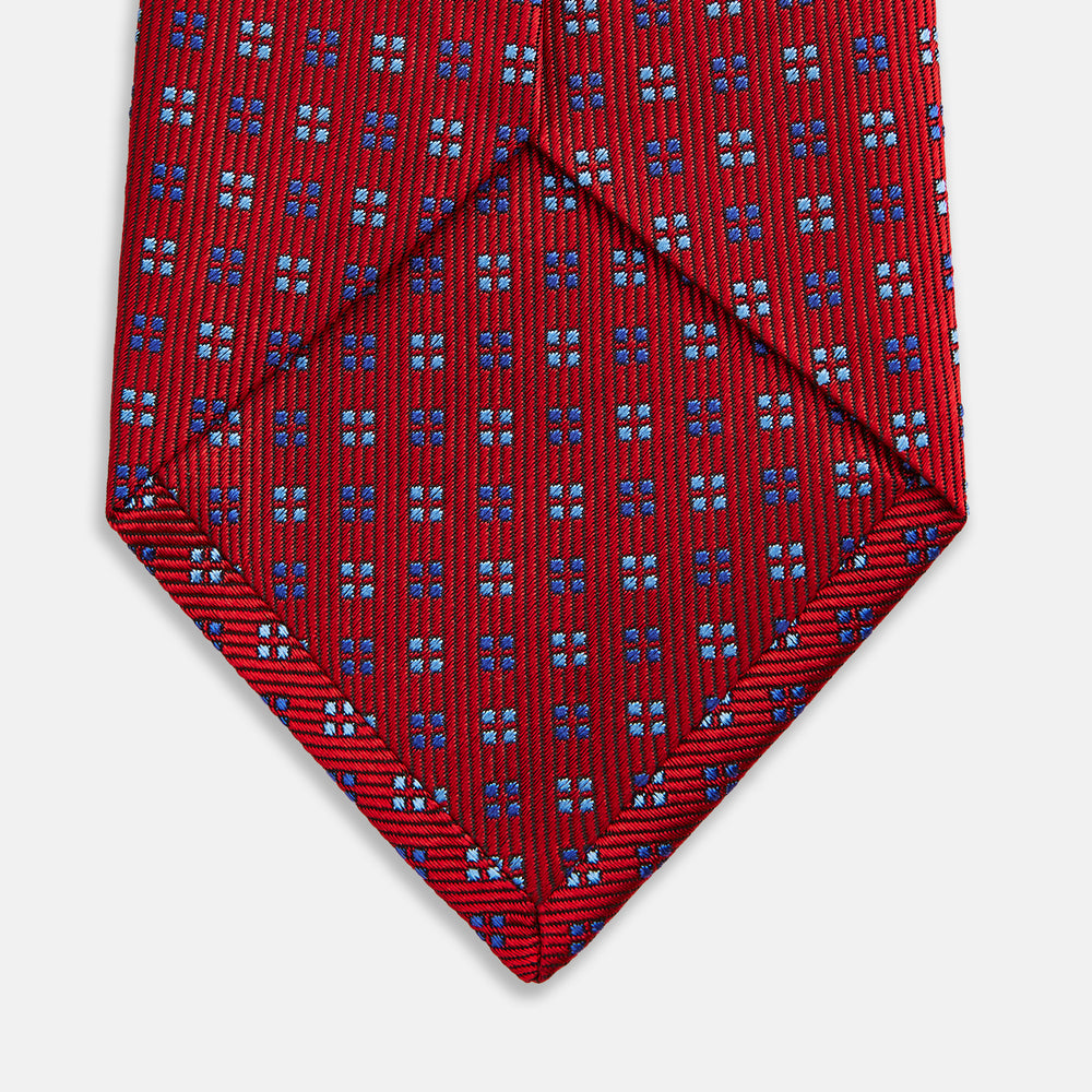 The Turnbull & Asser MINI SQUARE SPOT TULIP RED BLUE TIE features a vivid red base with blue and white geometric spots, making it a stylish addition to any refined ensemble.