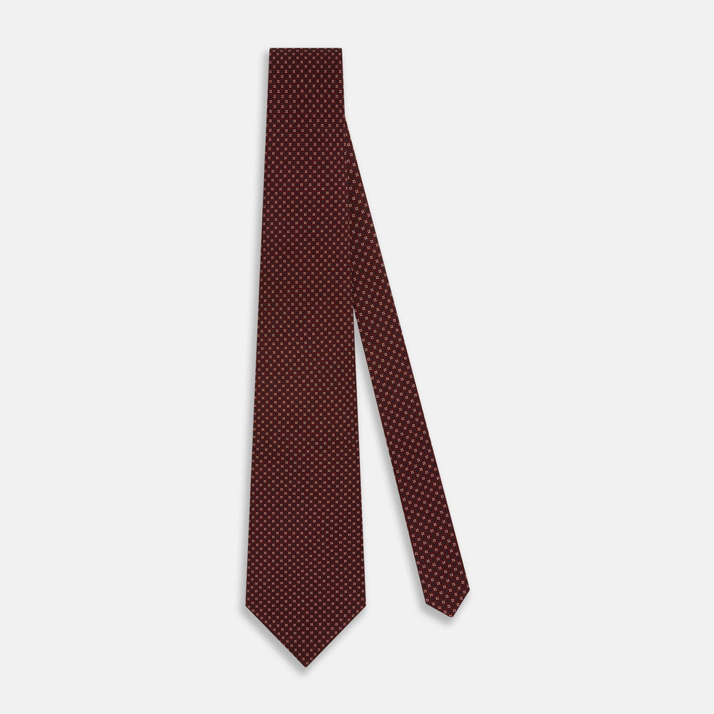 The Burgundy Geometric Motif Silk Tie by Turnbull & Asser features blue and white dots and is displayed neatly rolled on a plain white background.