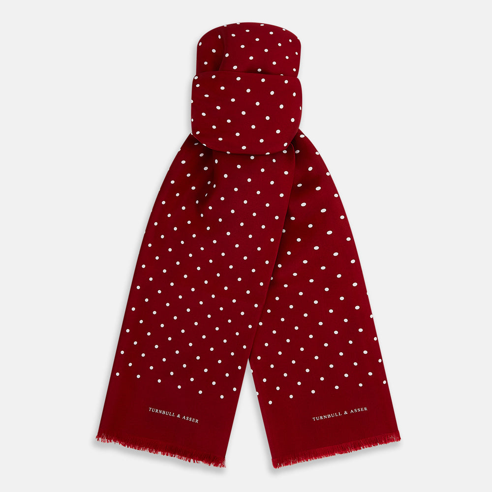 The Burgundy and White Spotted Silk Scarf by Turnbull & Asser features a gradient of white polka dots, short fringed edges, and the brand's name near the ends—a timeless classic foulard.