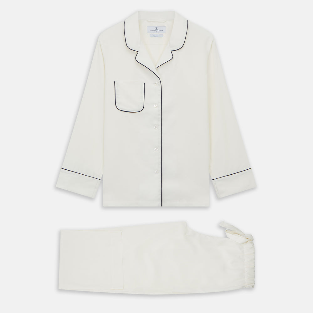 The Women's Harriet Cream Silk Pyjama Set by Turnbull & Asser features a white sand-washed silk button-up top with black piping and chest pocket, plus matching drawstring pants, all shown against a white background.