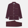 View 1 of product The Turnbull & Asser Plain Plum Silk Modern Pyjama Set, made in England, features white piping, a button-up long-sleeve top with three pockets, and matching pants. The pyjamas are shown against a white background.