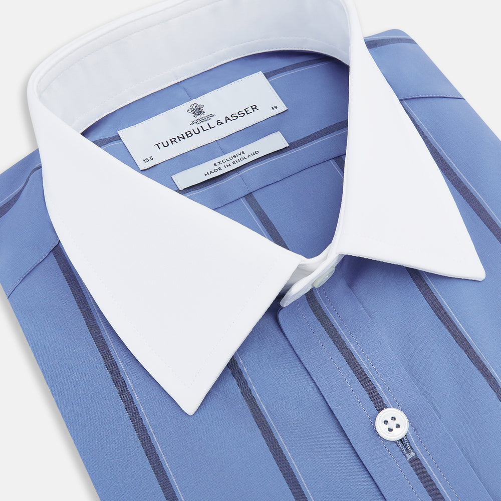 The Turnbull & Asser Colony Blue Track Stripe Shirt features vertical dark blue stripes, a Mayfair fit, and contrast white T&A collar and cuffs, reflecting British craftsmanship against a plain light background.