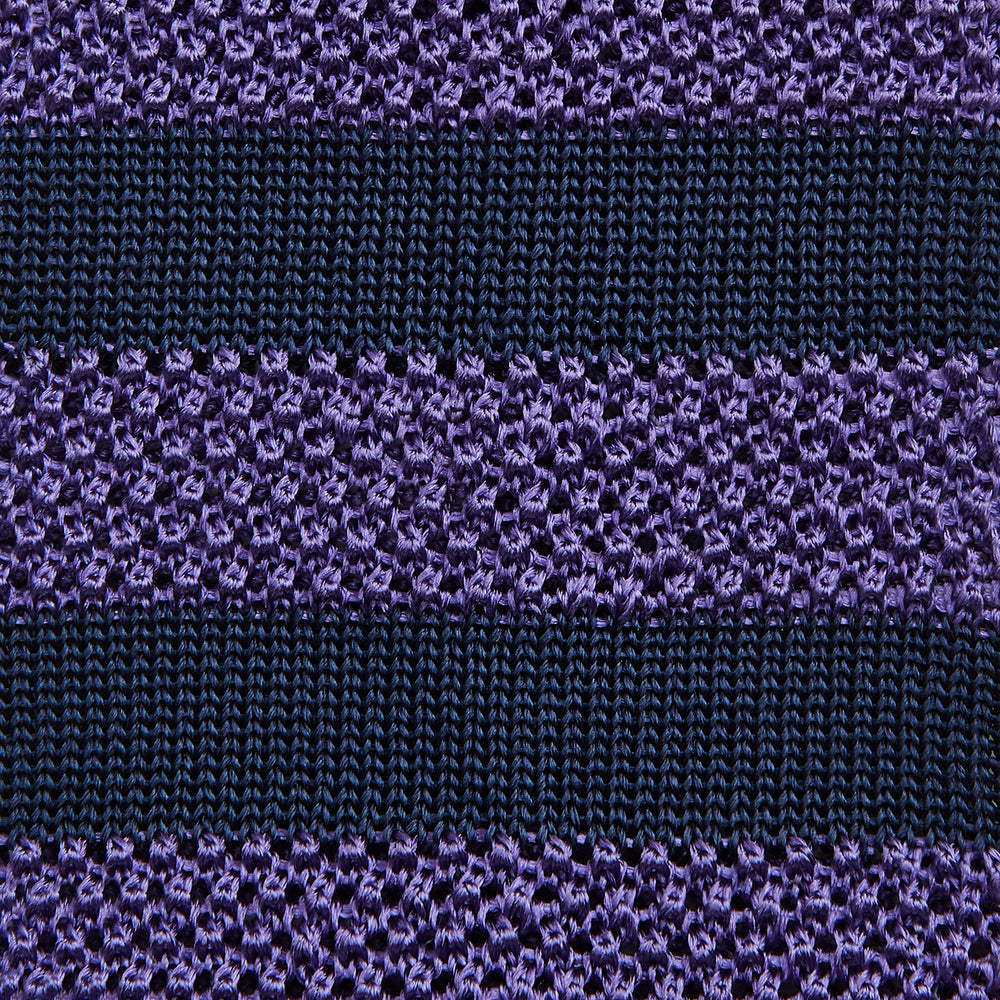 The KNITTED STRIPE PURPLE TIE by Turnbull & Asser features bold dark blue and purple stripes, making it an essential smart accessory. Shown rolled up on a white background.