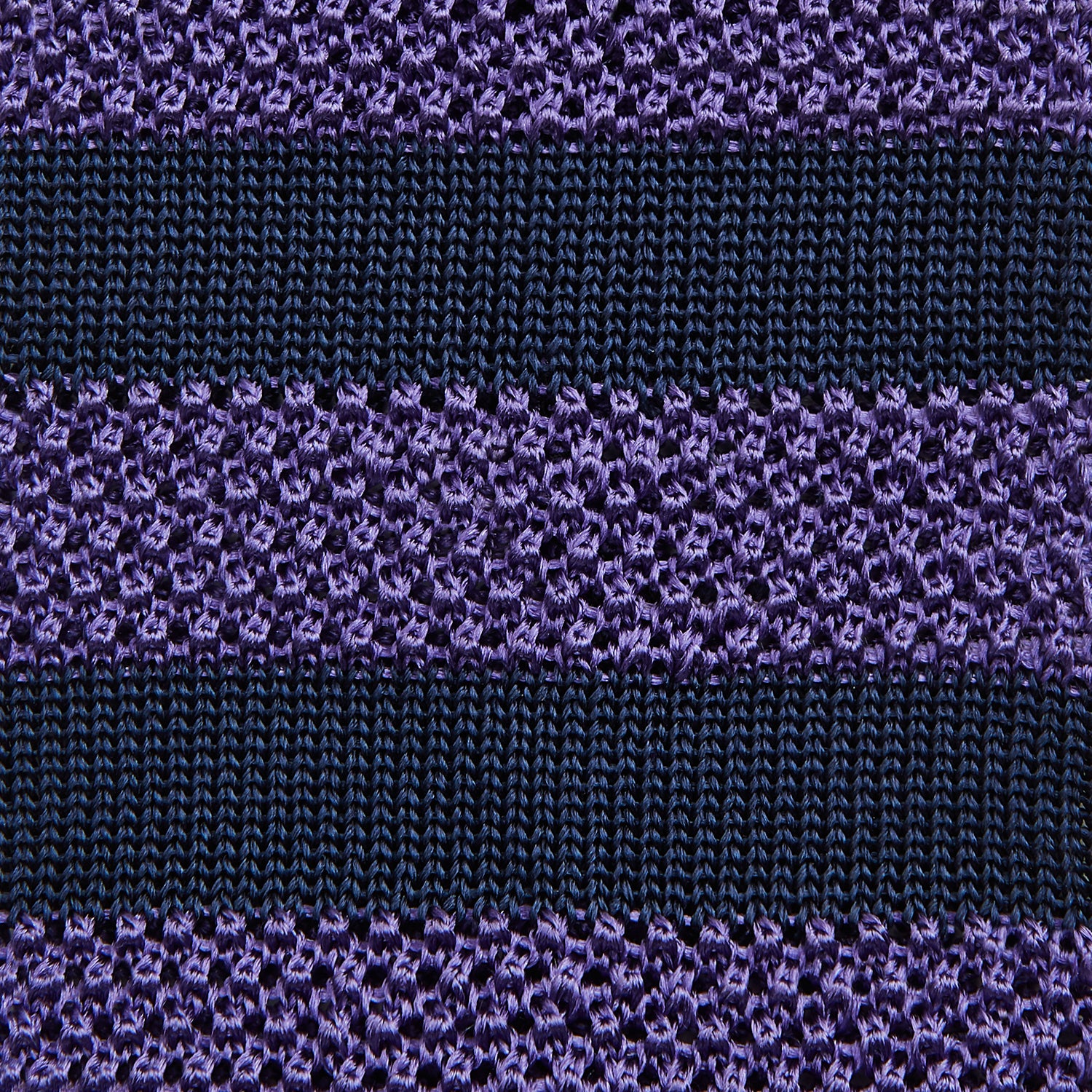 View 3 of product The KNITTED STRIPE PURPLE TIE by Turnbull & Asser features bold dark blue and purple stripes, making it an essential smart accessory. Shown rolled up on a white background.