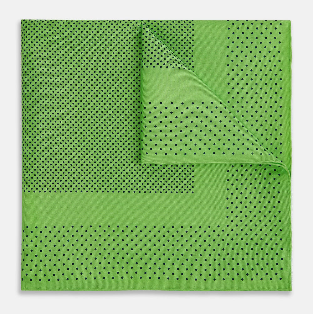 The Fern Green Dot Silk Pocket Square by Turnbull & Asser is crafted from pure silk, featuring a subtle black polka dot border with a denser dot pattern at the center and the brand name printed in the upper right corner.