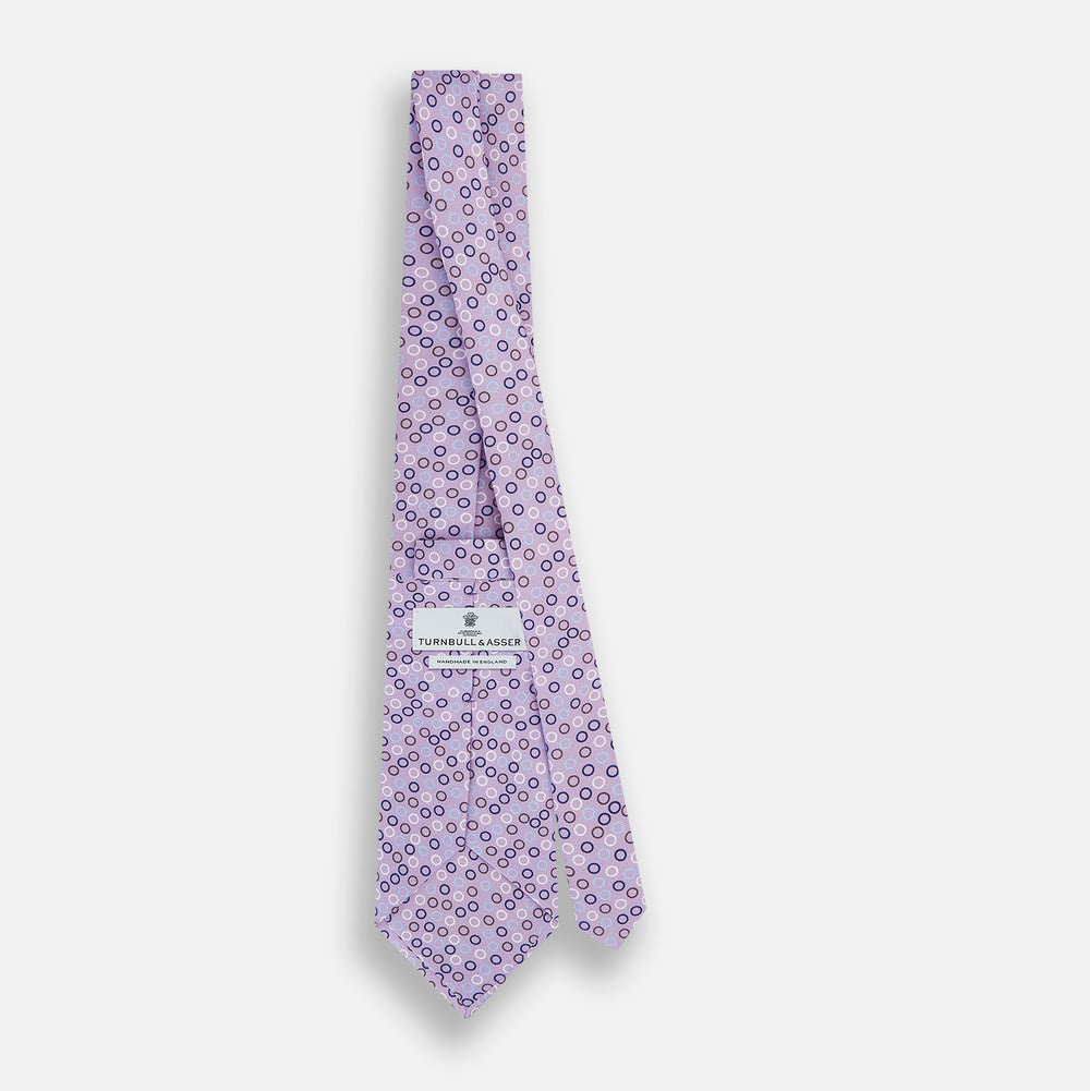 The Turnbull & Asser Multi-coloured Circle Lilac Silk Tie features overlapping blue, purple, and white circles on fine English silk—ideal for elevating smart outfits. Shown rolled against a plain white background.