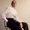 View 9 of product A woman stands in profile, looking down with hands in her pockets, wearing the Turnbull & Asser Turnbull and The Deck White Cotton Expressionist Shirt, paired with high-waisted black-and-white houndstooth pants.