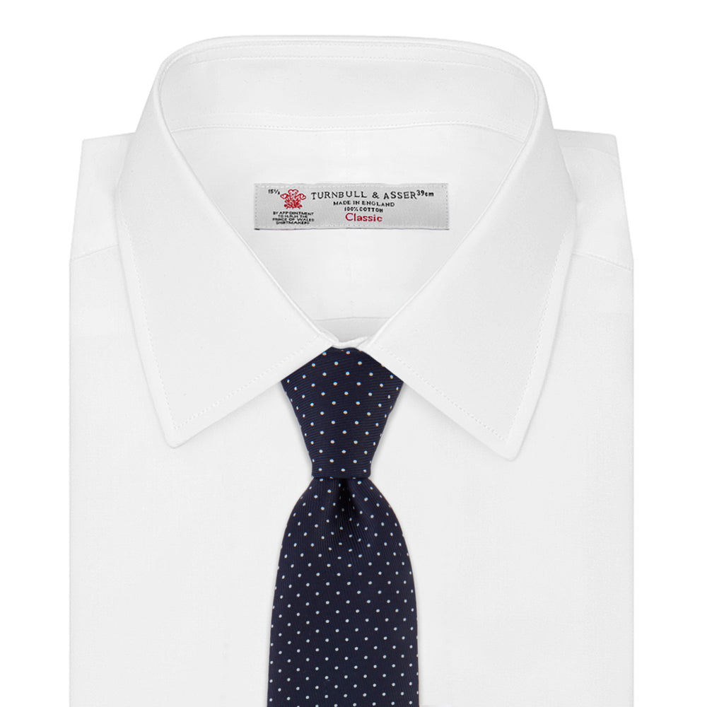 The Turnbull & Asser White and Navy Spot Printed Silk Tie, shown rolled with its pointed end forward on a white background, is an elegant accessory that pairs perfectly with a crisp shirt for smart occasions.