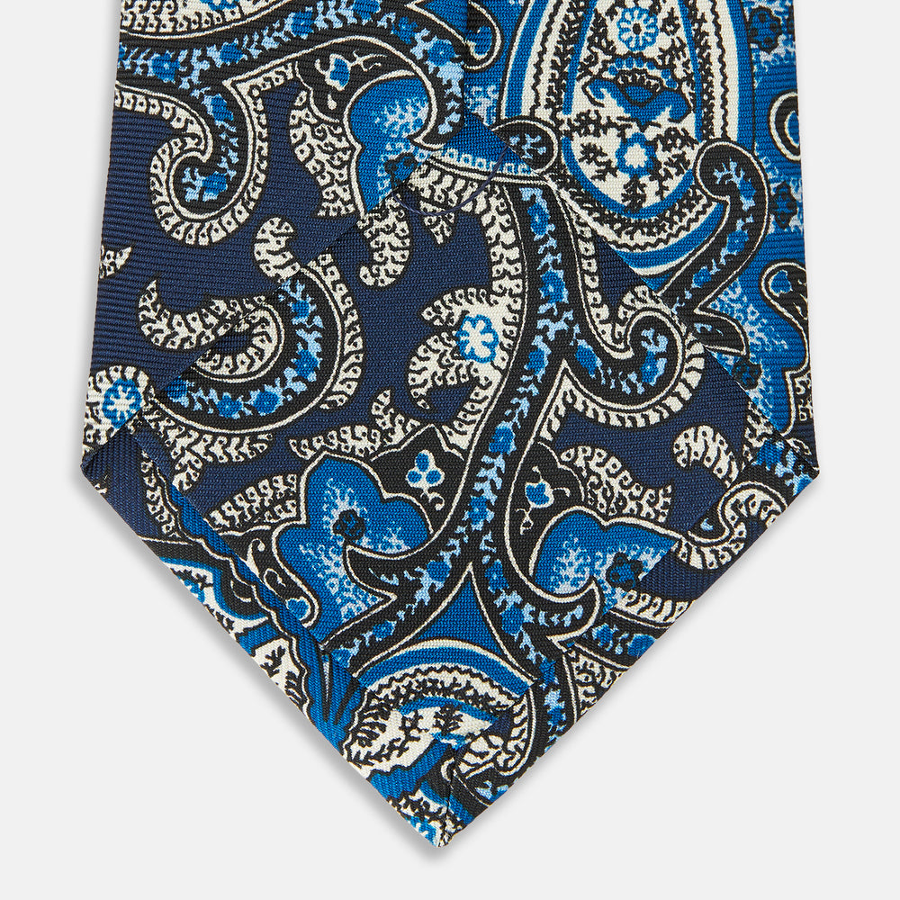 The Turnbull & Asser Blue and Navy Twisted Paisley Silk Tie displays intricate blue, white, and black details, rolled up against a plain white background.