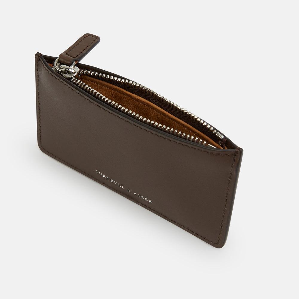 The Dark Chocolate Leather Zip Wallet by Turnbull & Asser, crafted from full-grain Italian leather, features a white brand logo on the front and is displayed against a plain white background.