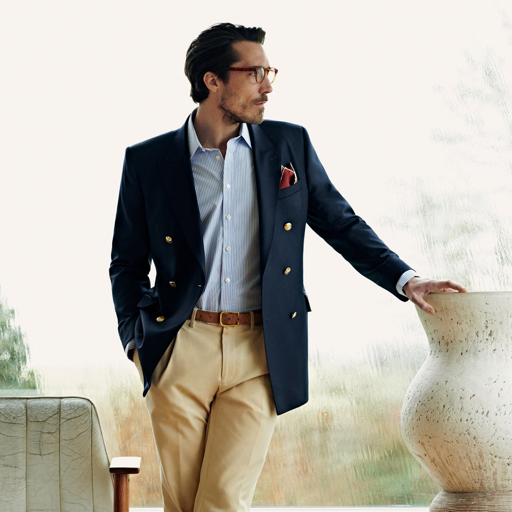 The Classic Navy Wool Blazer by Turnbull & Asser features a double-breasted design, gold buttons, notched lapels, and multiple front pockets, shown on a white background. This piece offers timeless, sophisticated nautical style.
