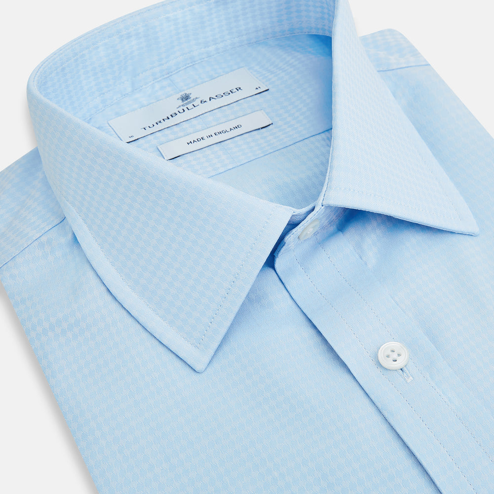 The Pale Blue Rhombus Mayfair Shirt by Turnbull & Asser features long sleeves, a classic collar, white buttons, and buttoned cuffs, shown laid flat on a white background.