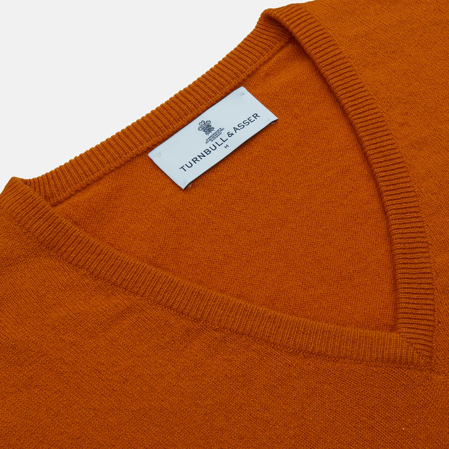 View 2 of product The Turnbull & Asser Rust Paden V-Neck Jumper, a pure cashmere sweater with long sleeves and ribbed cuffs and hem, is laid flat on a white background with the label visible at the neck.