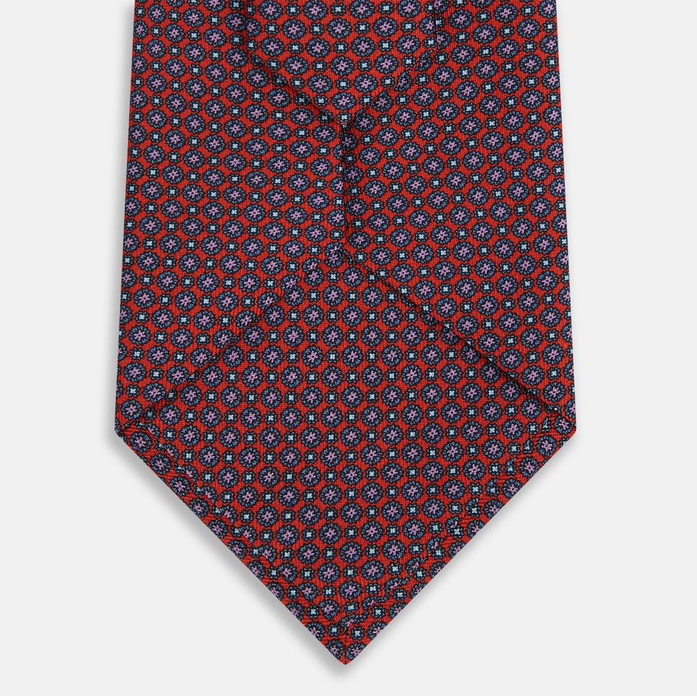 The Red Multi-Floral Silk Tie by Turnbull & Asser features a blue and white geometric pattern and is shown rolled up against a plain white background.