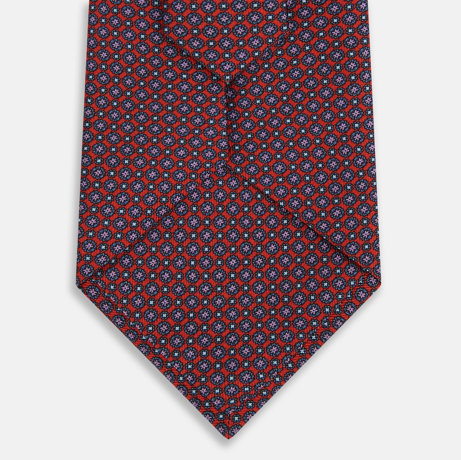 View 3 of product The Red Multi-Floral Silk Tie by Turnbull & Asser features a blue and white geometric pattern and is shown rolled up against a plain white background.