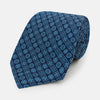 View 1 of product The Turnbull & Asser Dark Navy Floral Tile Pattern Printed Silk Tie, rolled up and displayed on a white background, features a blue geometric and floral pattern.