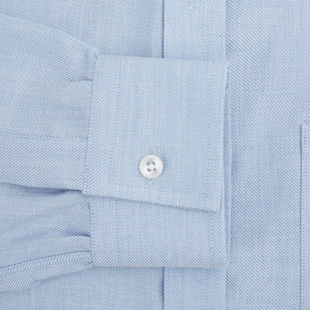The Turnbull & Asser Pale Blue Cotton Cashmere Derby Collar Richmond Shirt features a soft cotton-cashmere blend, derby collar, white buttons, left chest pocket, and buttoned cuffs, shown laid flat on a white background.