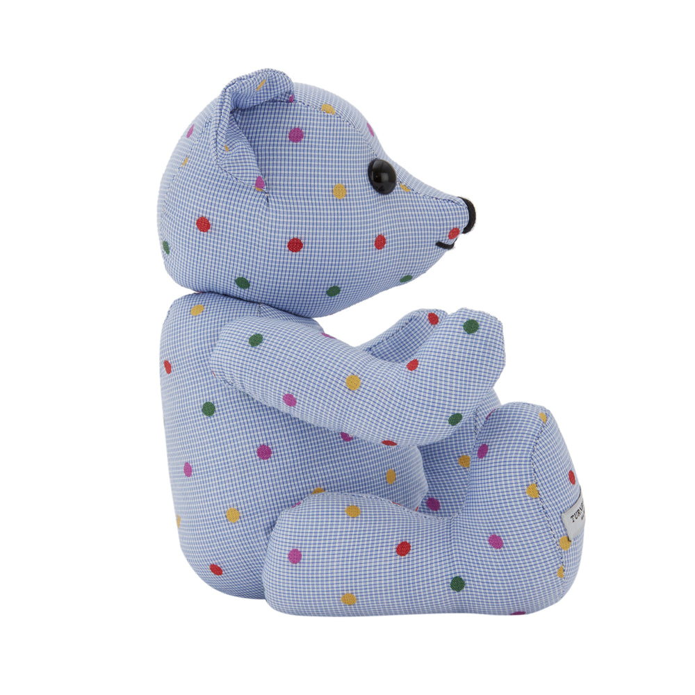 The Turnbuline Cotton Spot Teddy Bear by Turnbull & Asser is a blue gingham bear with colorful polka dots, black button eyes, a black nose, and a white leg label, shown sitting upright in profile facing left.