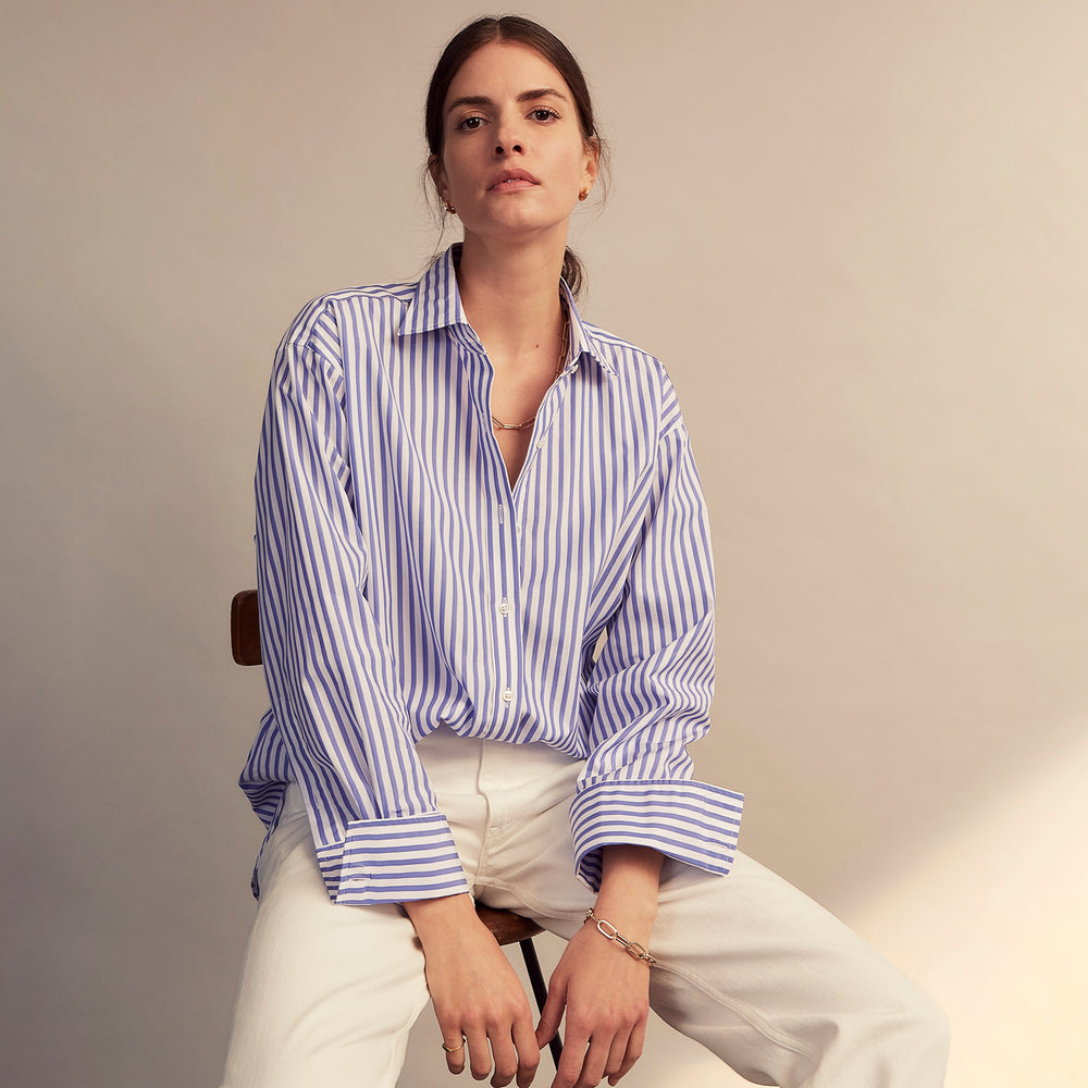 The Turnbull & Asser Pale Blue Candy Stripe Cotton Marlene Shirt is an oversized women's collared shirt with long sleeves, buttoned cuffs, and vertical blue and white stripes, shown laid flat on a white background.