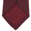 View 4 of product The Turnbull & Asser Plain Woven Grenadine Silk Tie, shown rolled at one end on a white background, features a rich burgundy hue and textured pattern—an essential accessory for sophisticated looks.