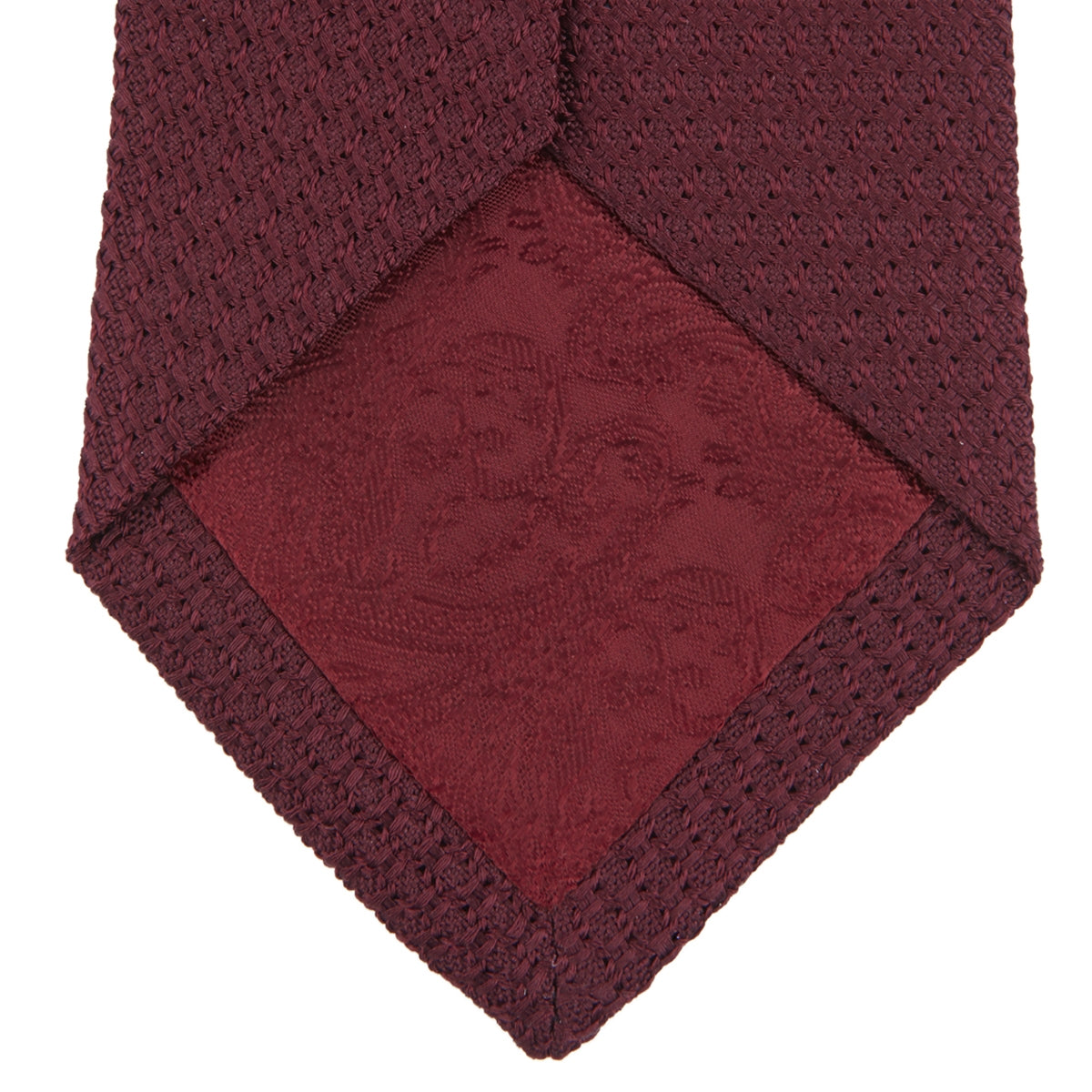 View 4 of product The Turnbull & Asser Plain Woven Grenadine Silk Tie, shown rolled at one end on a white background, features a rich burgundy hue and textured pattern—an essential accessory for sophisticated looks.
