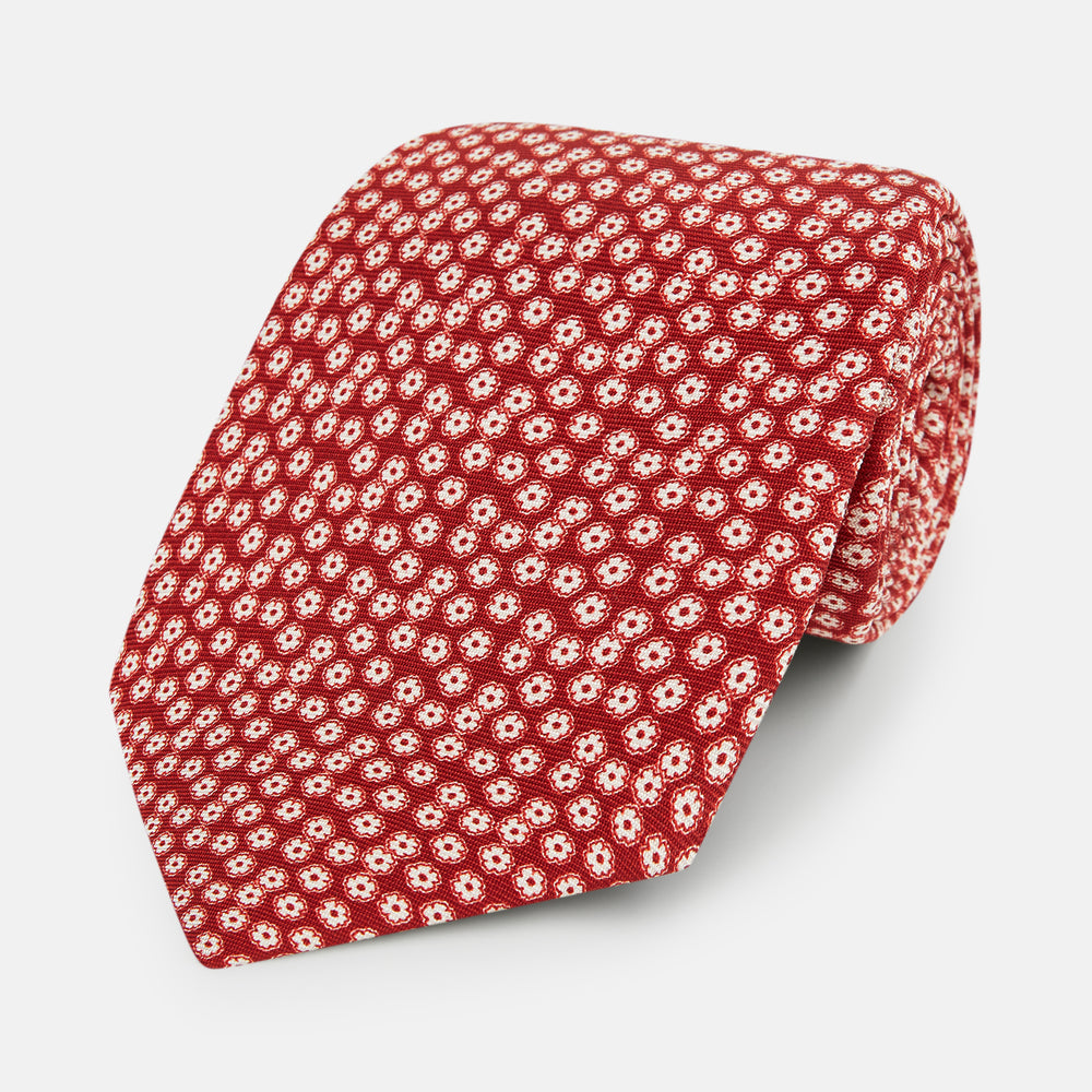 The Turnbull & Asser Red Flower-Patterned Printed Silk Tie, made from fine English silk, features a repeating white floral design and is shown rolled on a plain white background.