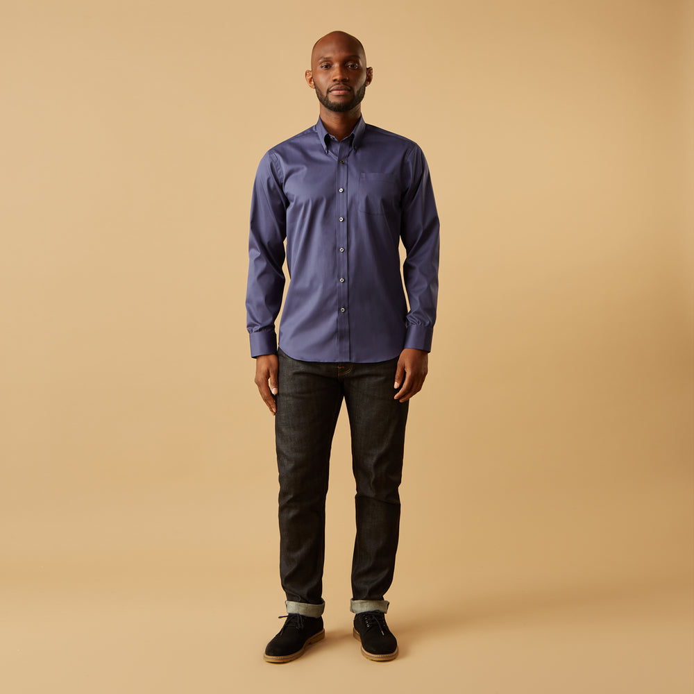 The Blue Piece Dyed Weekend Fit Suffolk Shirt by Turnbull & Asser features a button-down Dorset collar, chest pocket, white buttons, and long sleeves in classic navy, laid flat against a white background.