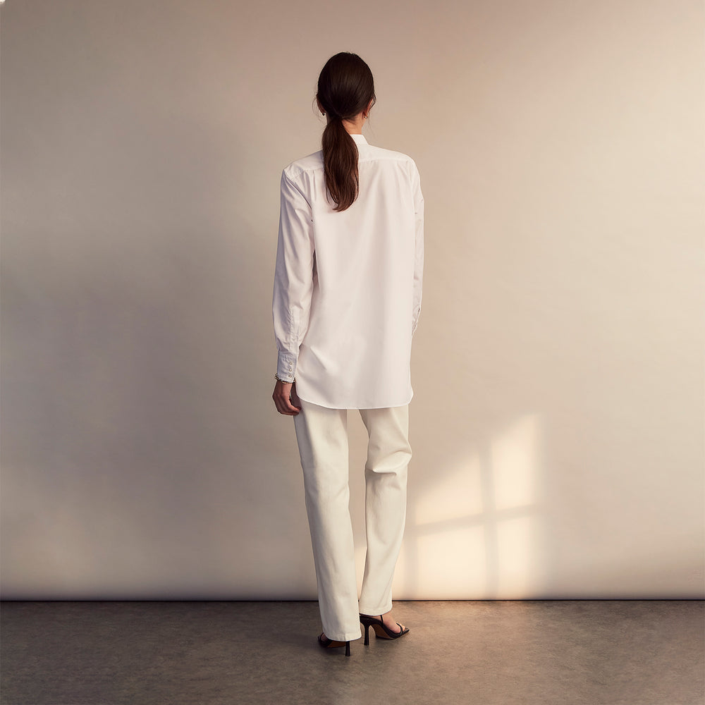 The White Cotton Lauren Shirt by Turnbull & Asser, featuring a stand collar, button-down front, and elongated body, is laid flat on a plain white background.