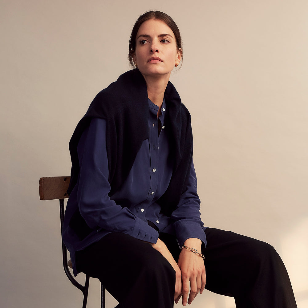The Turnbull & Asser Blue Soft-touch Silk Lauren Shirt is a navy, long-sleeve button-up with an Igret stand collar, white buttons, curved hem, relaxed fit, and elongated body for a modern look, shown laid flat on a white background.
