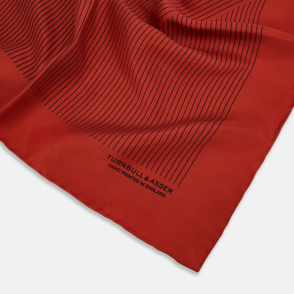 The Red Stripe Silk Pocket Square by Turnbull & Asser features thin black vertical lines and the brand signature in black on one corner, with a neatly folded edge for a touch of classic British style.
