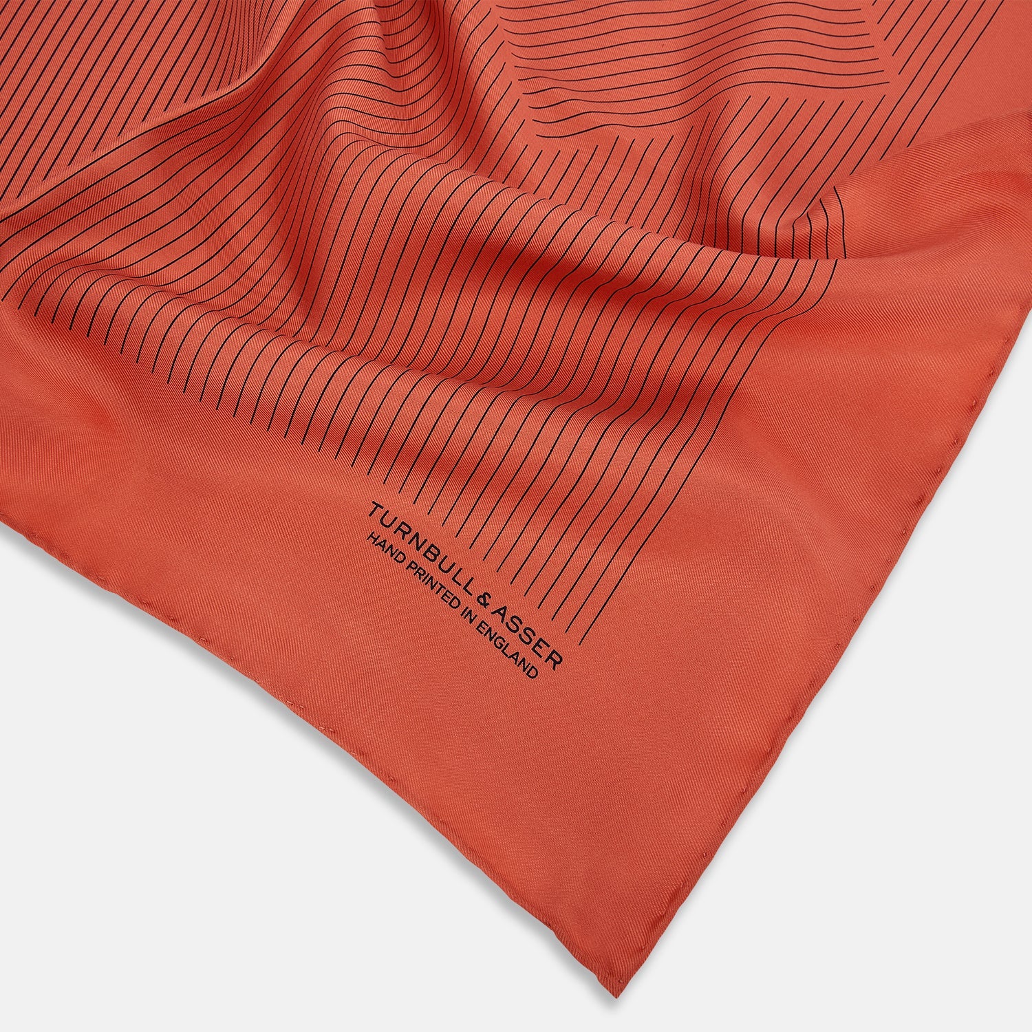 View 2 of product The Orange Stripe Silk Pocket Square by Turnbull & Asser features thin black vertical lines and "TURNBULL & ASSER HAND PRINTED IN ENGLAND" in the corner, neatly folded on a white background.