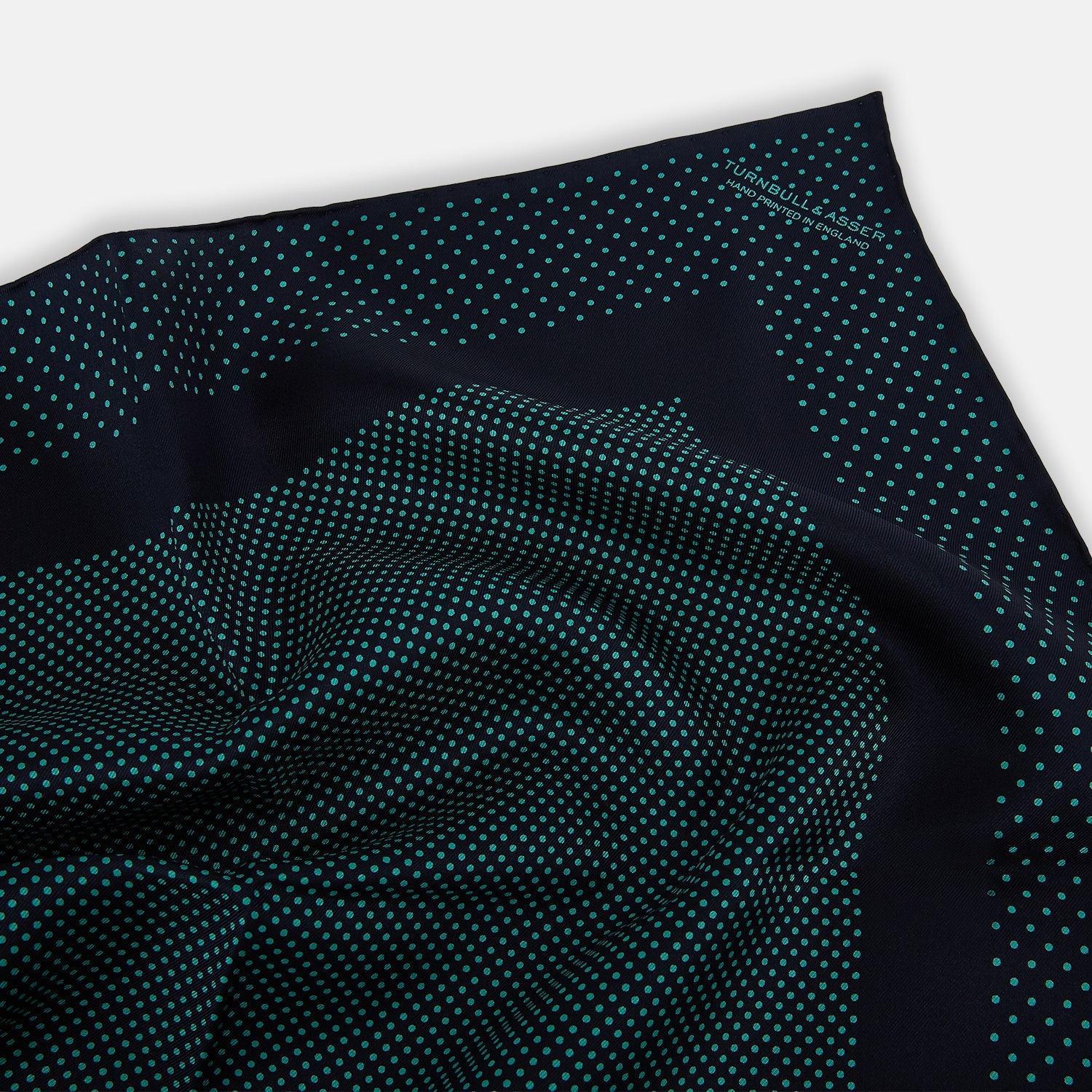 View 2 of product The Turnbull & Asser Navy and Petrol Green Dot Silk Pocket Square features handmade craftsmanship with petrol green polka dots and a darker border, elegantly displayed on a white background.